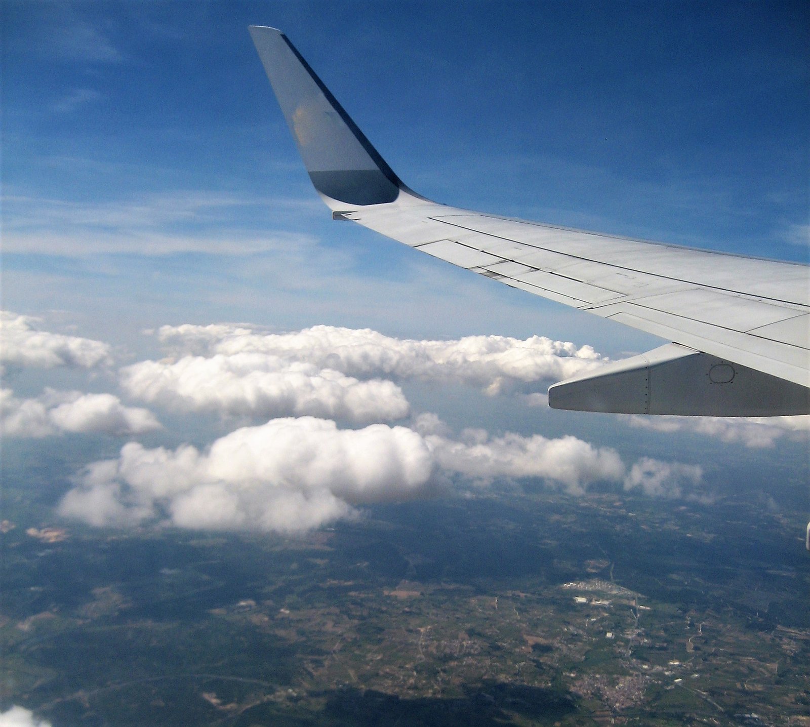 Uitzicht uit een raam van een vliegend vliegtuig. Je ziet vleugel, wolke en de aarde.